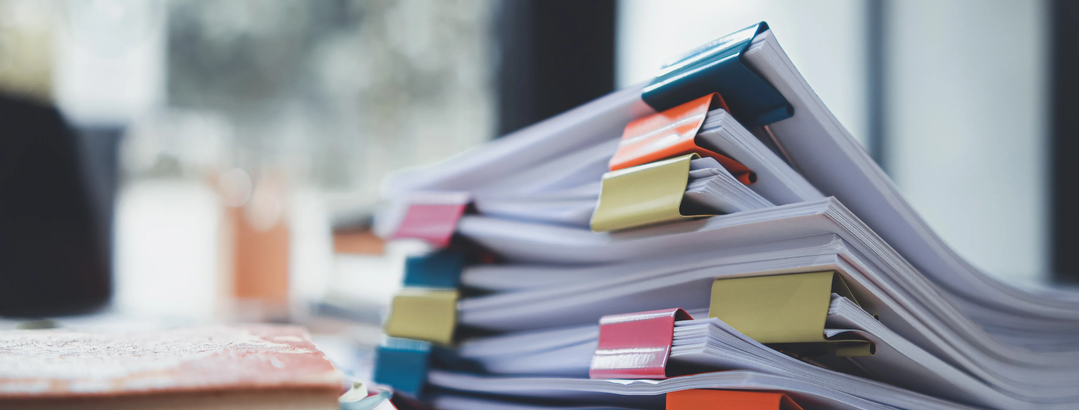 stack of photos clipped together with brightly colored binder clips on a desk in front of a window