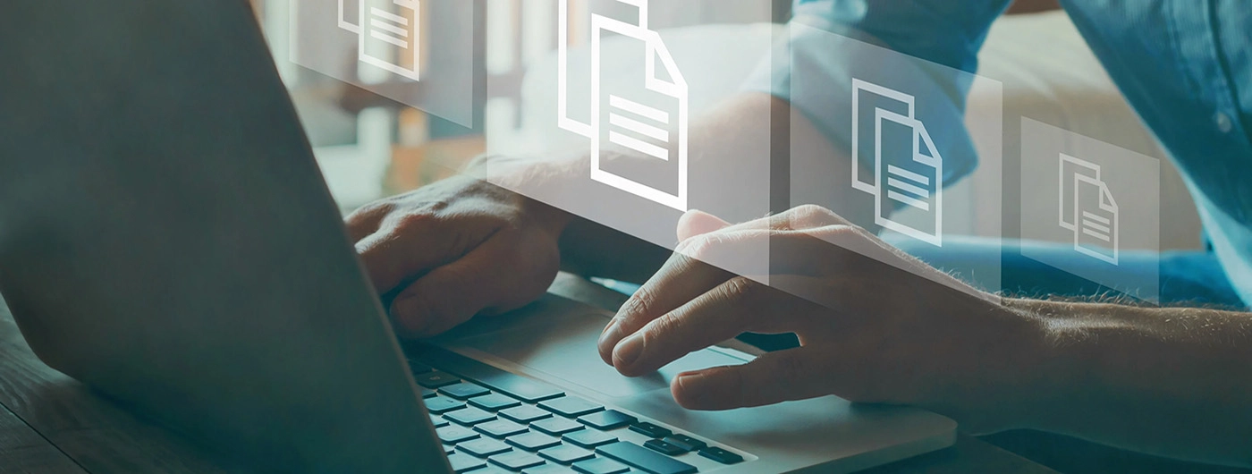 Close up of hands typing on a laptop with document icons being shown transparently over their hands