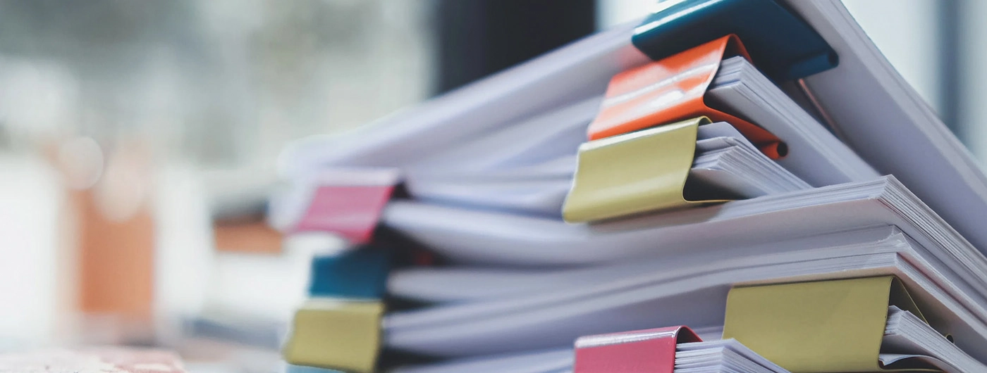 stack of photos clipped together with brightly colored binder clips on a desk in front of a window